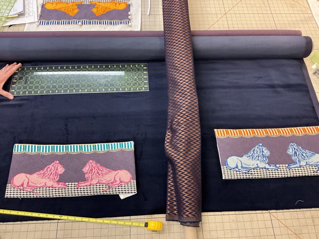 A roll of dark fabric is laid out on a work surface with a ruler, a tape measure, and two lion patterned fabric samples in pink and blue.